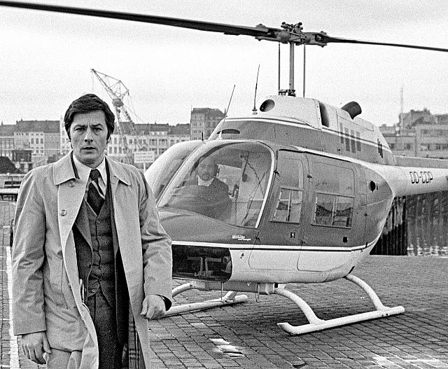Alain Delon au premier plan lors du tournage du film Armaguedon. Hector Lecomte se trouve aux commandes du Bell 206A Jet Ranger OO-CDP, en 1977 - Photo DR